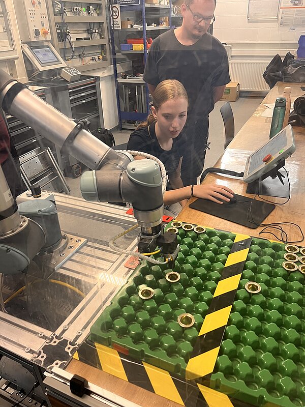 Roboterarm und Studentin am Arbeitsplatz